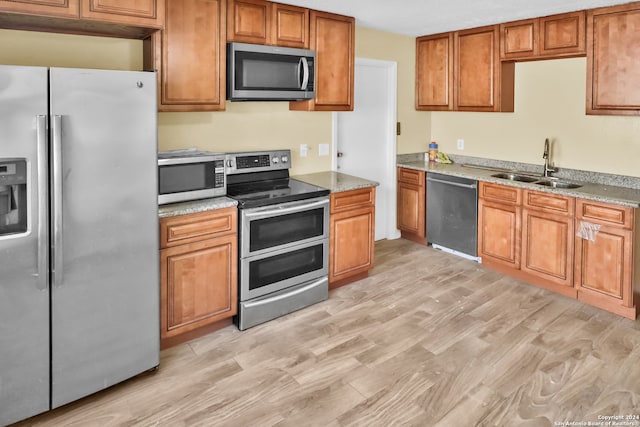 kitchen featuring light wood-type flooring, appliances with stainless steel finishes, light stone counters, and sink