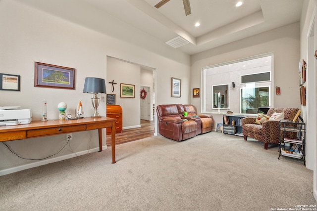 living room with a raised ceiling, ceiling fan, and light colored carpet