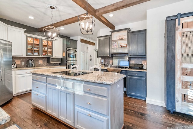 kitchen with a barn door, hanging light fixtures, stainless steel appliances, and dark hardwood / wood-style flooring