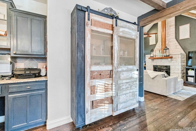 kitchen featuring beamed ceiling, dark hardwood / wood-style flooring, a fireplace, tasteful backsplash, and a barn door