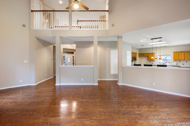 unfurnished living room with ceiling fan, dark hardwood / wood-style flooring, and a high ceiling