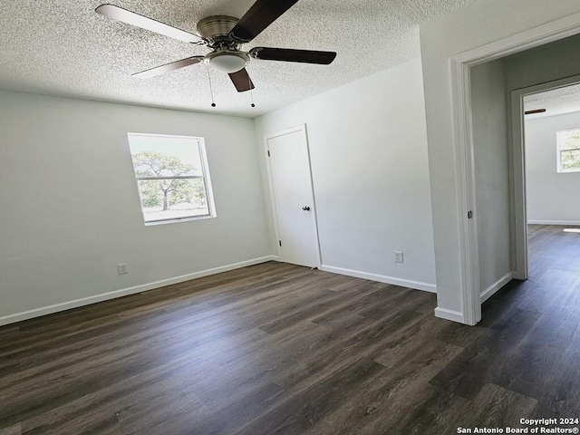 unfurnished bedroom with a textured ceiling, multiple windows, dark wood-style flooring, and baseboards