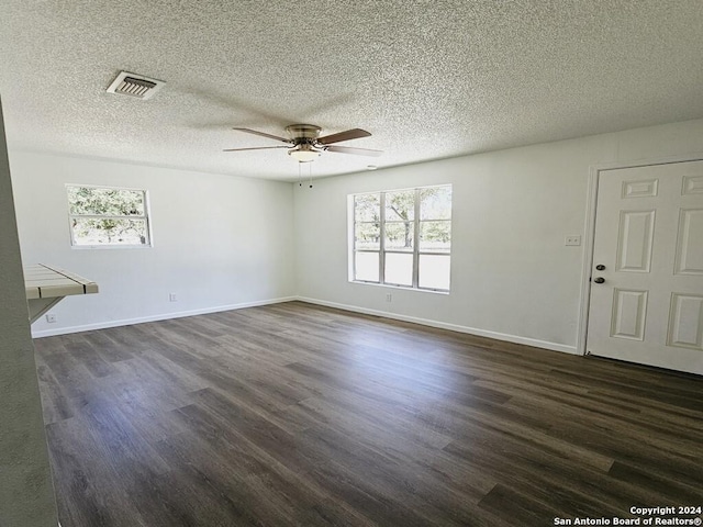 empty room featuring visible vents, dark wood-type flooring, and a wealth of natural light