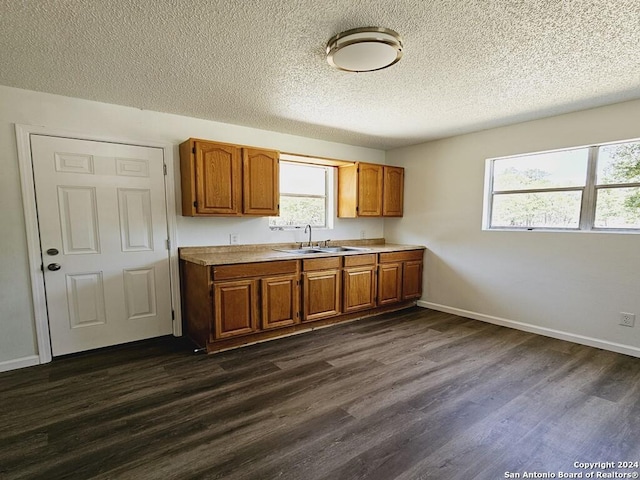 kitchen with brown cabinetry, dark wood-style flooring, light countertops, and a sink