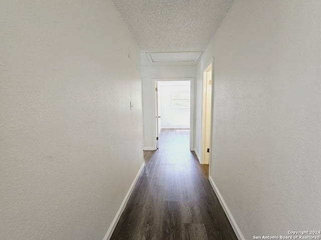 corridor featuring dark wood-style floors, attic access, a textured ceiling, and baseboards