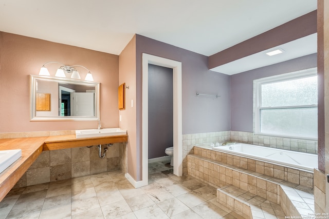 bathroom with tile patterned flooring, tiled tub, toilet, and sink