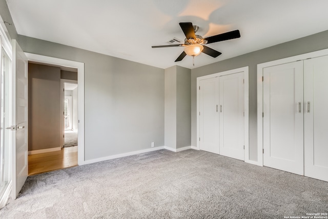 unfurnished bedroom with light carpet, two closets, and ceiling fan