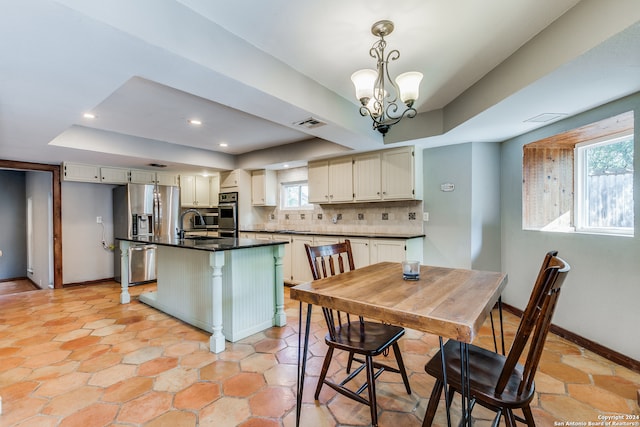 kitchen with a raised ceiling, stainless steel refrigerator with ice dispenser, light tile patterned floors, a kitchen island with sink, and decorative backsplash