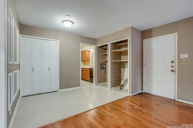 unfurnished bedroom with sink, two closets, ensuite bathroom, and light hardwood / wood-style flooring