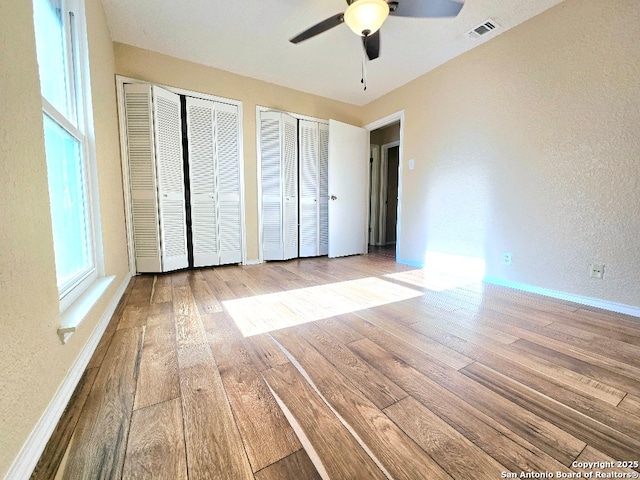 unfurnished bedroom featuring baseboards, hardwood / wood-style floors, visible vents, and multiple closets