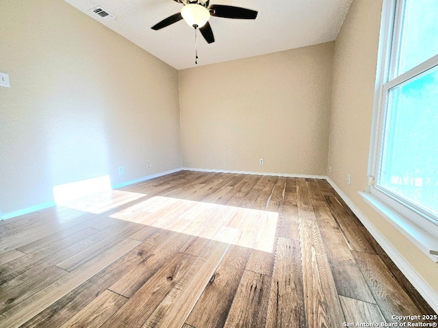 empty room featuring a ceiling fan, baseboards, visible vents, and wood finished floors