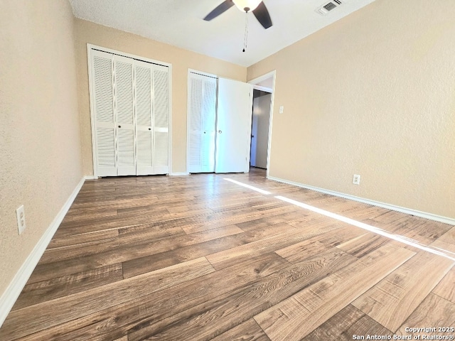 unfurnished bedroom featuring baseboards, wood finished floors, visible vents, and multiple closets