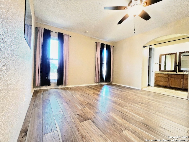 unfurnished room with a textured ceiling, a textured wall, a ceiling fan, baseboards, and light wood-style floors