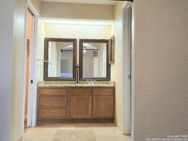 bathroom with double vanity, tile patterned flooring, a sink, and a textured wall