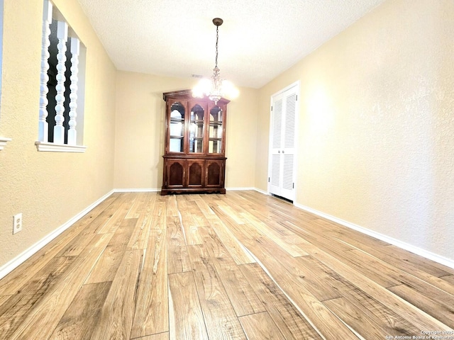 unfurnished dining area featuring a textured ceiling, a textured wall, baseboards, light wood finished floors, and an inviting chandelier