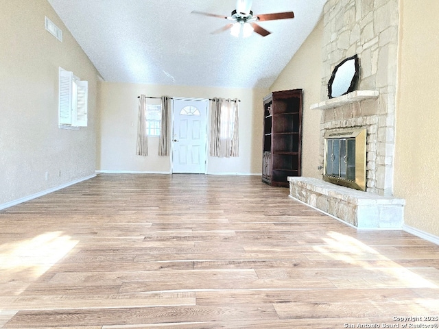 unfurnished living room featuring vaulted ceiling, a stone fireplace, wood finished floors, and visible vents