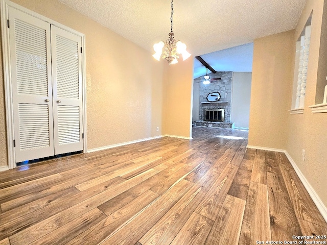 unfurnished dining area featuring a notable chandelier, a fireplace, lofted ceiling, a textured ceiling, and wood finished floors