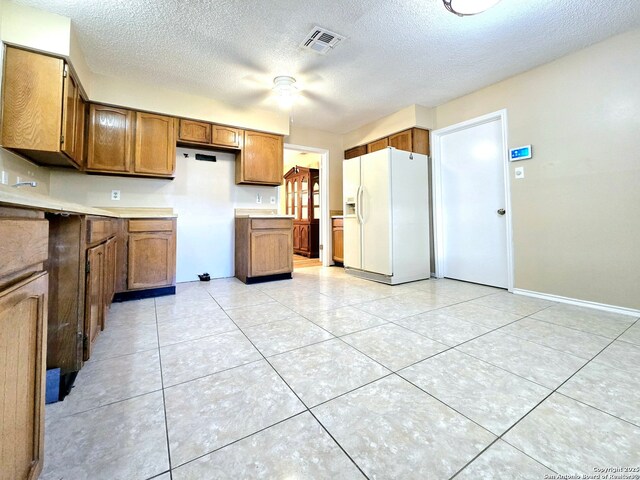 kitchen with a textured ceiling, ceiling fan, sink, white fridge with ice dispenser, and light tile patterned flooring