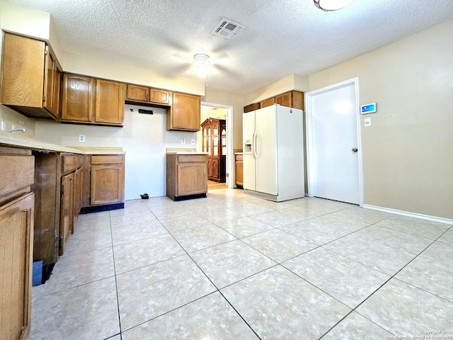 kitchen featuring white refrigerator with ice dispenser, visible vents, brown cabinets, a textured ceiling, and light tile patterned flooring