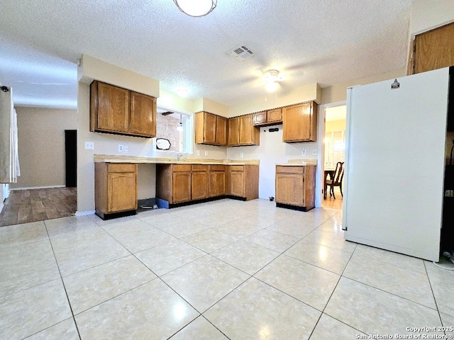 kitchen featuring visible vents, brown cabinets, freestanding refrigerator, light countertops, and a sink