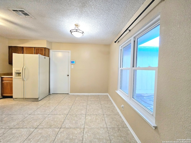 interior space with light tile patterned floors, baseboards, visible vents, brown cabinetry, and white fridge with ice dispenser