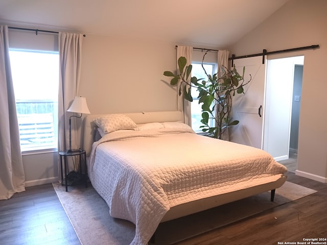 bedroom with a barn door, vaulted ceiling, and dark hardwood / wood-style floors