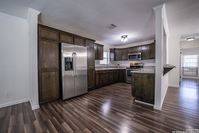 kitchen featuring ornamental molding, appliances with stainless steel finishes, dark brown cabinets, and dark hardwood / wood-style floors