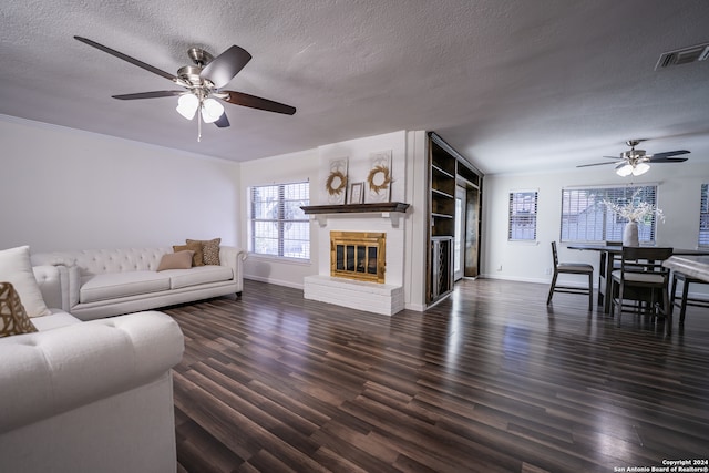 living room featuring a textured ceiling, dark wood-type flooring, ceiling fan, and a fireplace