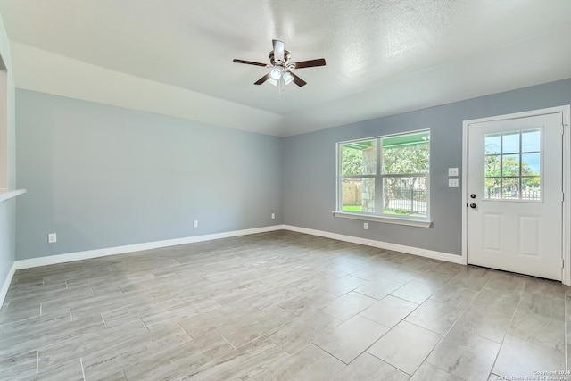 interior space with lofted ceiling, a textured ceiling, baseboards, and a ceiling fan