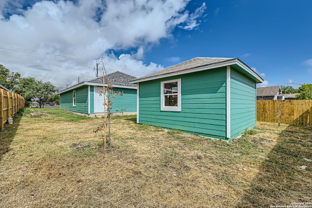 rear view of house with fence, an outdoor structure, and a yard