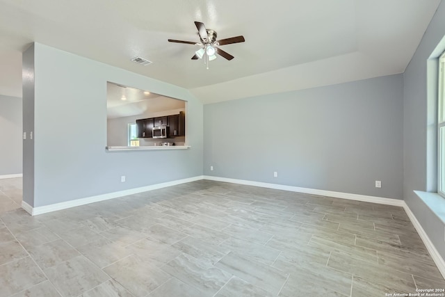 empty room with baseboards, vaulted ceiling, visible vents, and a ceiling fan