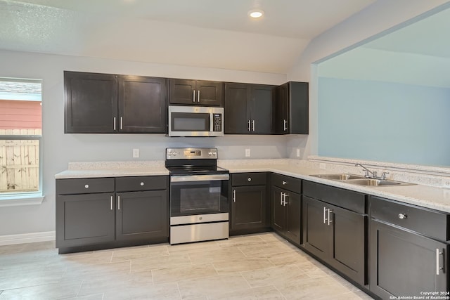 kitchen with lofted ceiling, appliances with stainless steel finishes, light countertops, a sink, and recessed lighting