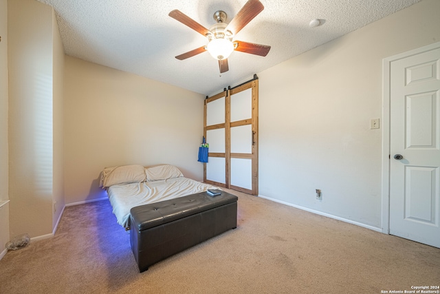 bedroom featuring carpet flooring, ceiling fan, a barn door, and a textured ceiling