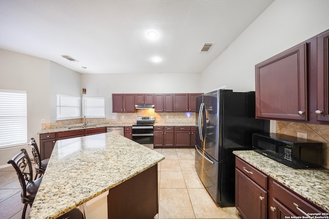 kitchen featuring backsplash, stainless steel appliances, light stone counters, a center island, and sink