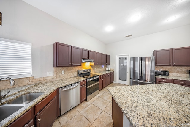 kitchen with light stone countertops, backsplash, appliances with stainless steel finishes, sink, and lofted ceiling