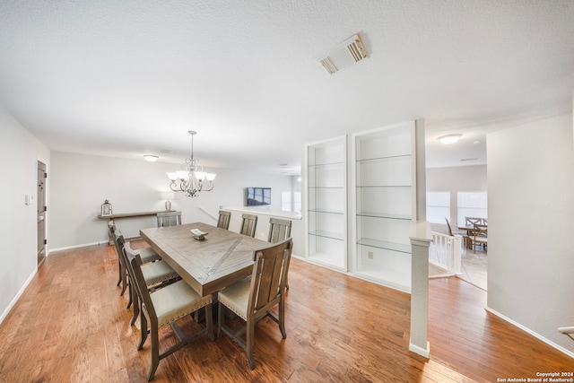 dining space with built in shelves, hardwood / wood-style flooring, a notable chandelier, and a textured ceiling