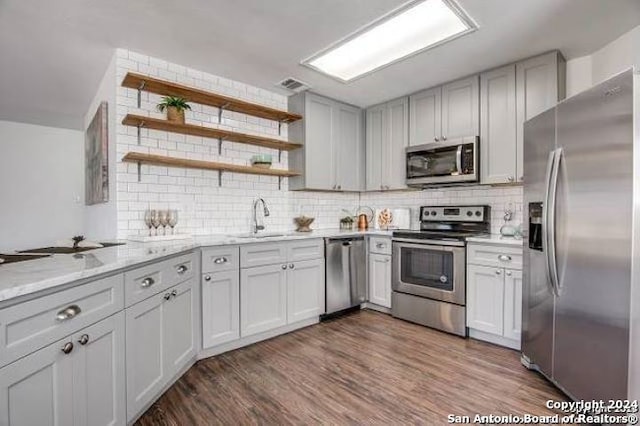 kitchen with backsplash, hardwood / wood-style floors, light stone counters, stainless steel appliances, and sink