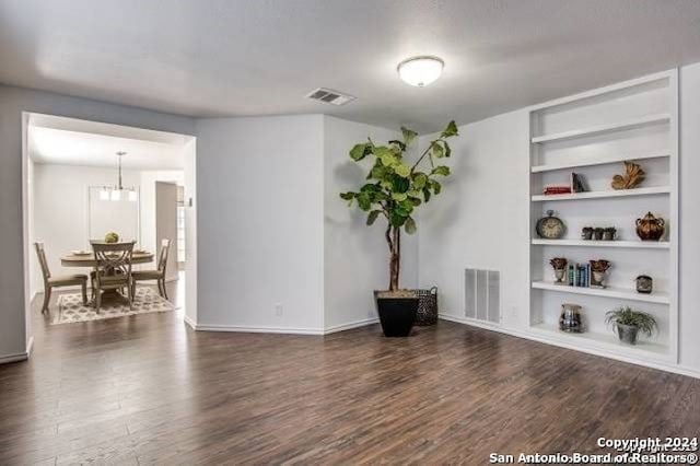 empty room featuring an inviting chandelier, built in shelves, and dark hardwood / wood-style floors