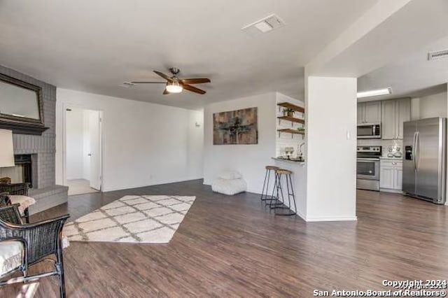 living room with ceiling fan, a brick fireplace, and dark hardwood / wood-style flooring