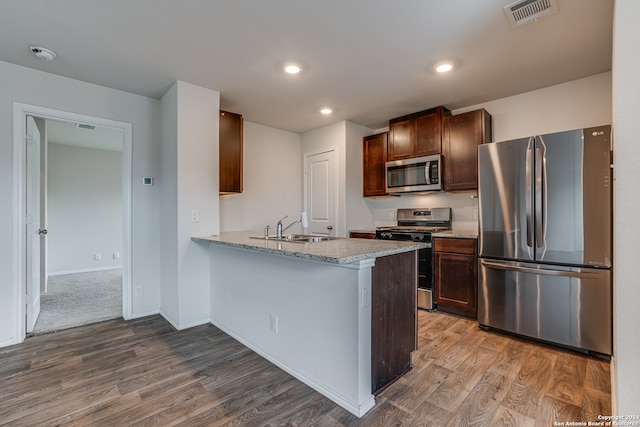 kitchen featuring hardwood / wood-style floors, appliances with stainless steel finishes, kitchen peninsula, sink, and light stone counters