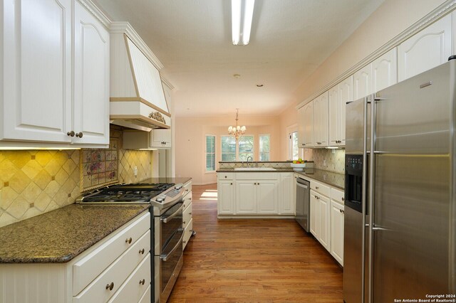 kitchen featuring stainless steel appliances, a peninsula, wood finished floors, a sink, and white cabinets