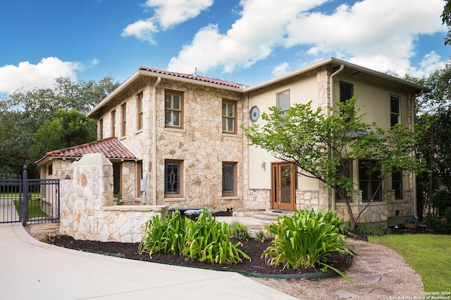 mediterranean / spanish-style home with stone siding, a tile roof, fence, and stucco siding