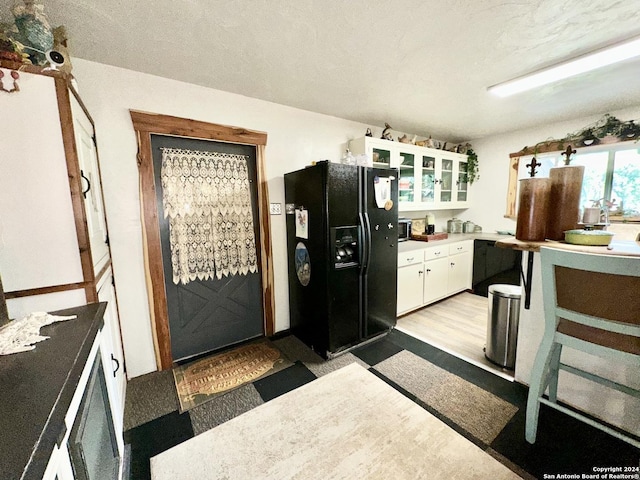 kitchen featuring light countertops, black fridge with ice dispenser, glass insert cabinets, white cabinets, and a textured ceiling