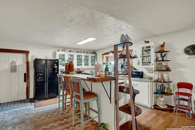 kitchen featuring light wood finished floors, glass insert cabinets, a textured ceiling, white cabinetry, and black fridge