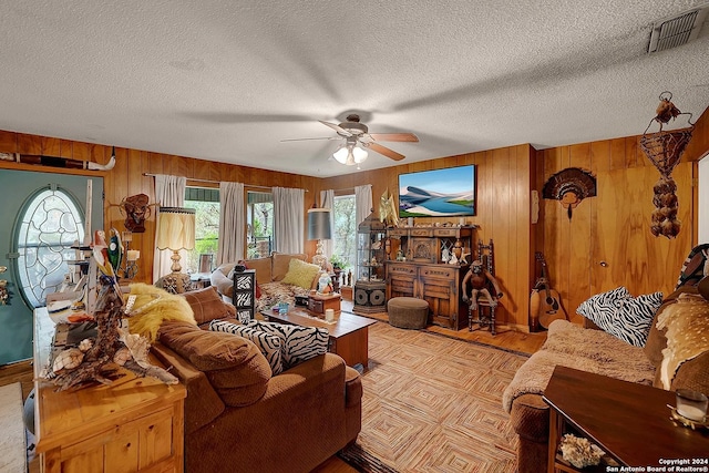 living area featuring ceiling fan, wood walls, a textured ceiling, and visible vents