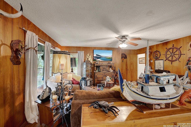 living room with a ceiling fan, visible vents, wood walls, and a textured ceiling