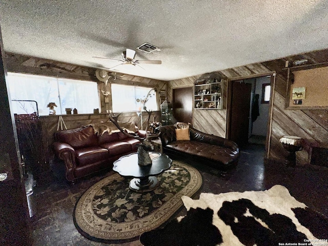 living area featuring a textured ceiling, a ceiling fan, visible vents, and wooden walls