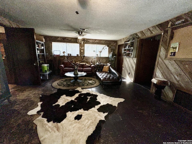 living room with ceiling fan, wooden walls, and a textured ceiling