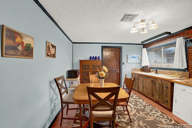 dining room with visible vents, ornamental molding, a textured ceiling, light wood-type flooring, and a notable chandelier