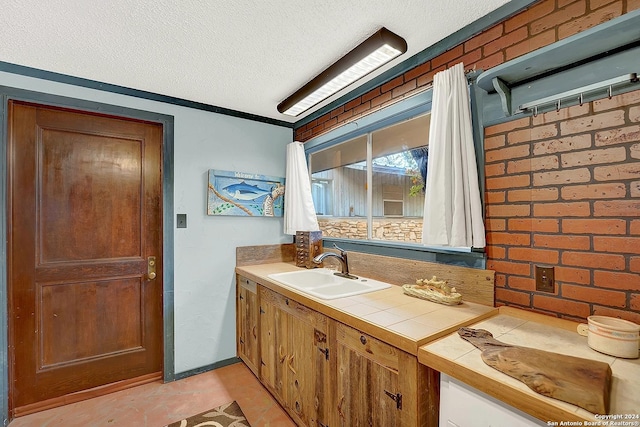 bathroom featuring a textured ceiling, brick wall, and vanity